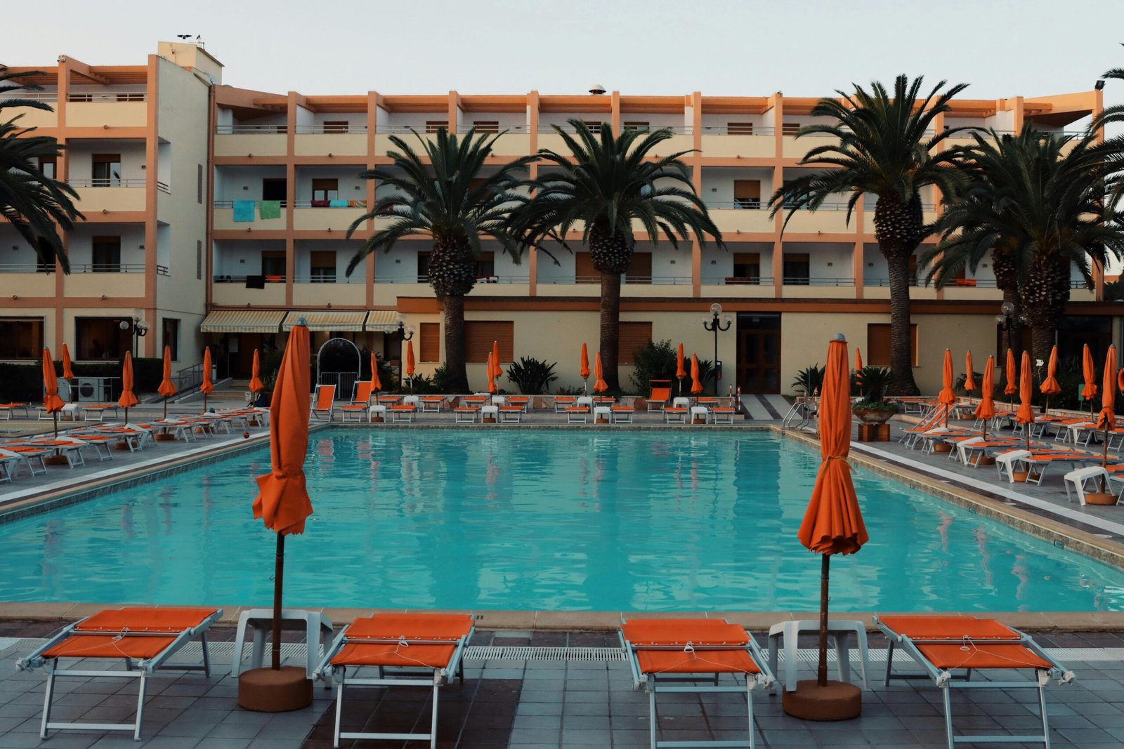 Empty poolside at a resort with palm trees and sunbeds in Alghero, Sardinia, ideal for a summer escape.